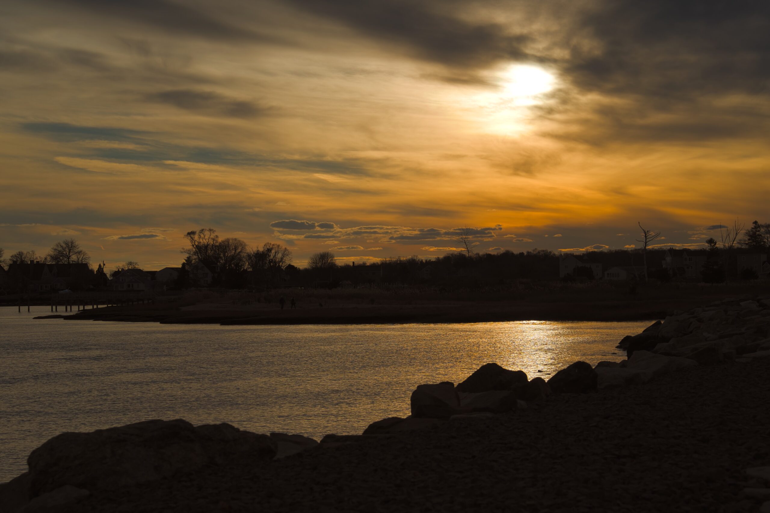 Golden light over the Guilford shoreline, with dark rocks in the foreground.