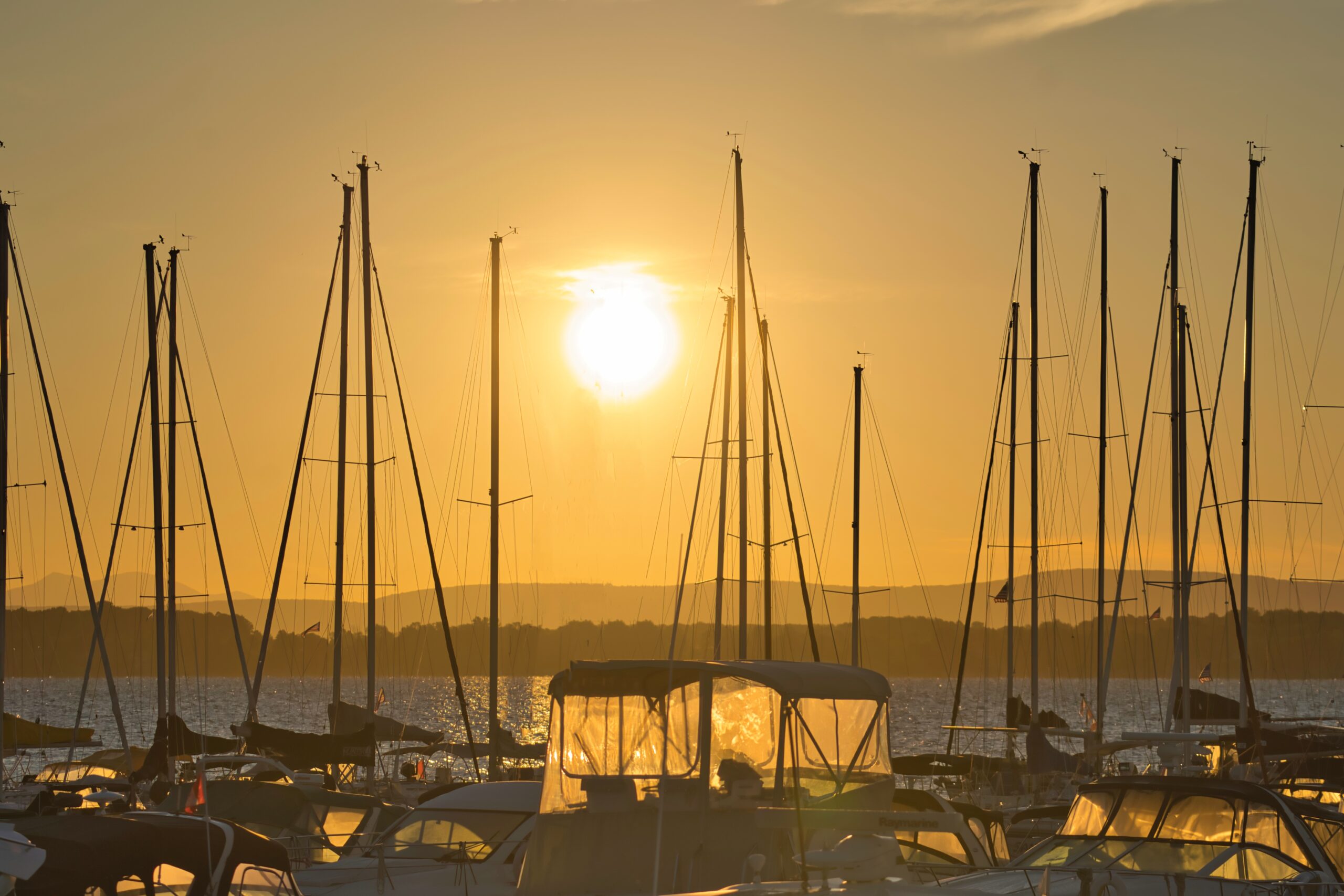 Golden sunrise shining through sailboat masts at a marina.