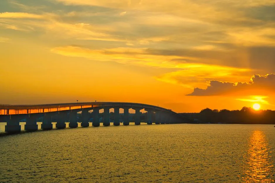A bridge silhouetted against a golden sunset over calm water.