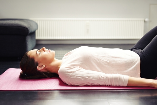 A woman resting on her back on a yoga mat with her knees bent.