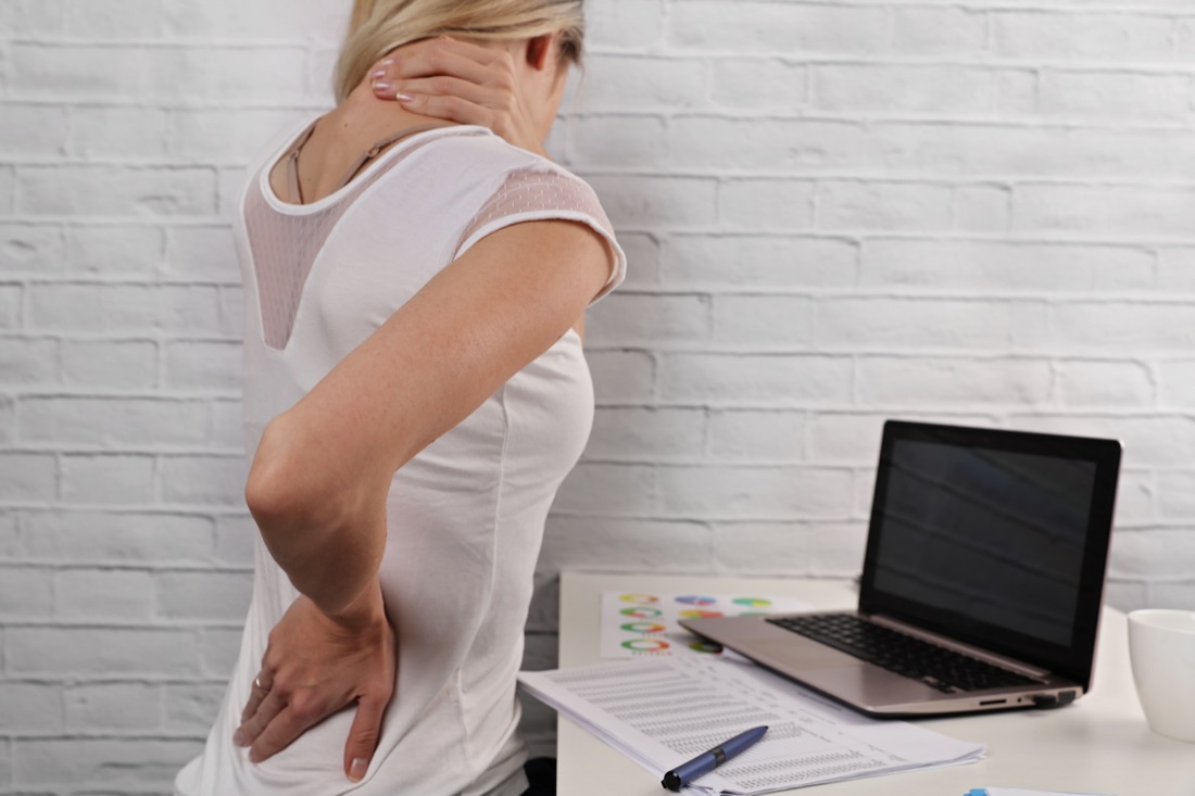 Woman beside a laptop with one hand on her neck and the other on her lower back.