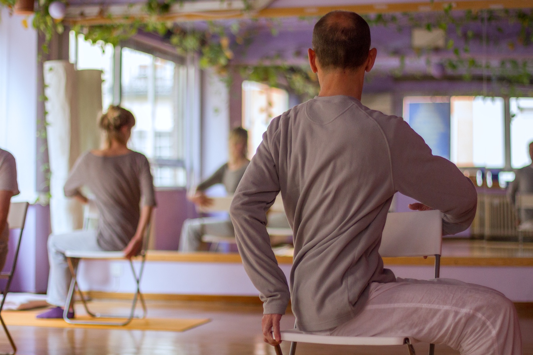 Adults practicing a seated turn on chairs in a yoga studio.