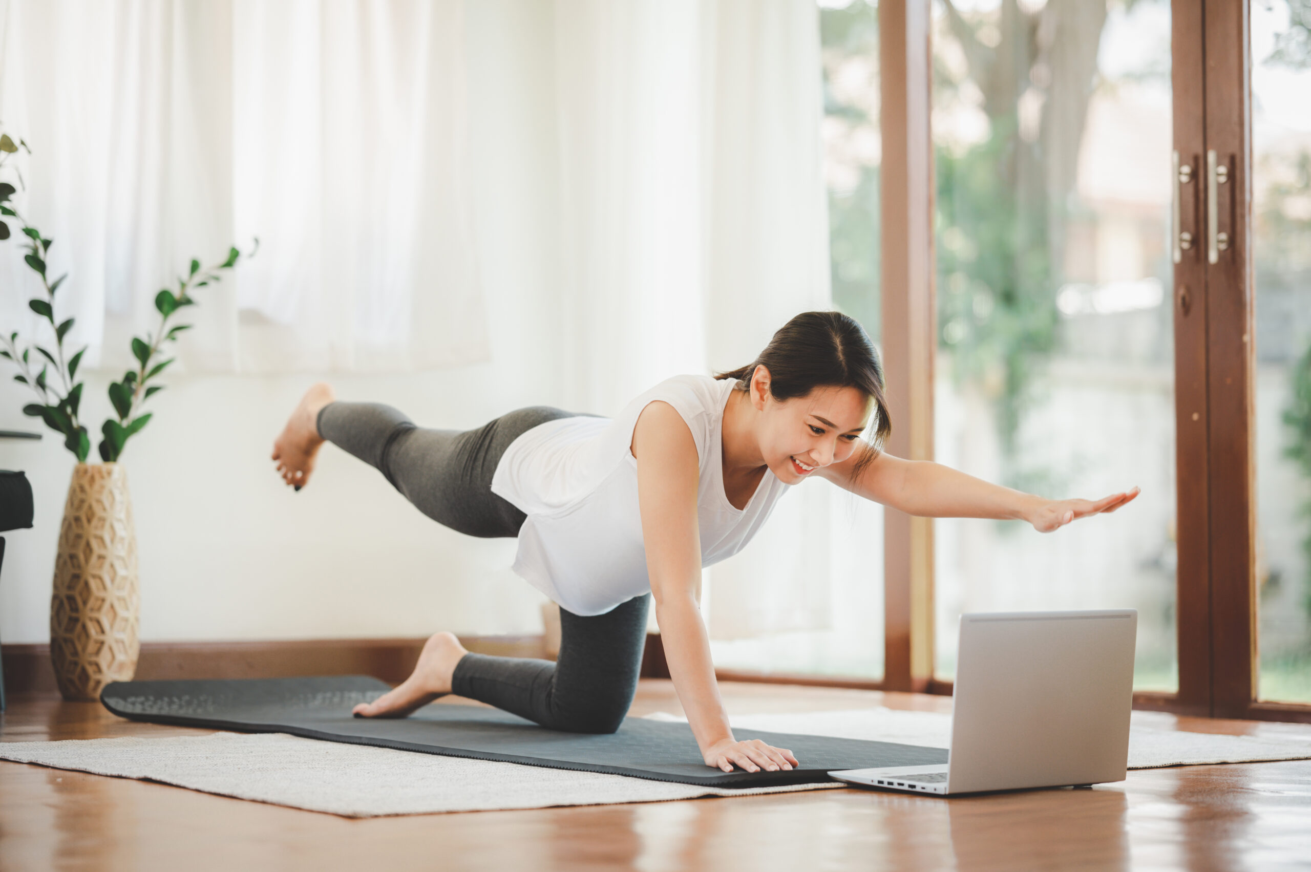 A woman extending one arm and the opposite leg from hands and knees beside a laptop.
