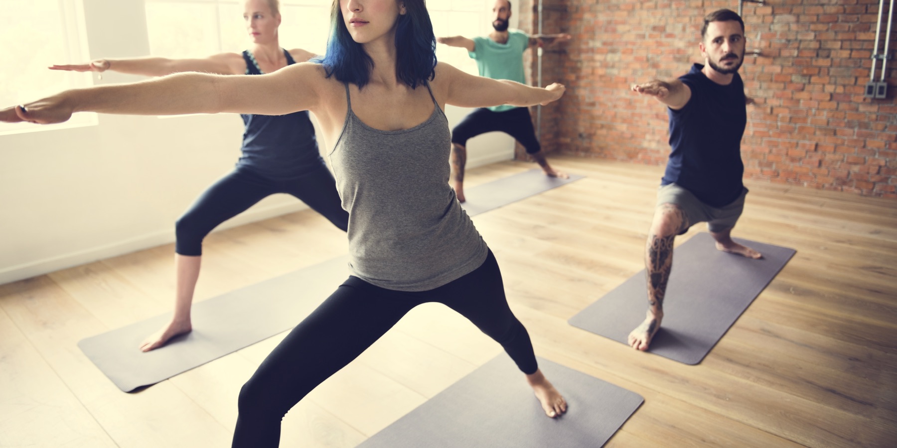 Adults practicing a standing yoga pose together in a bright studio.