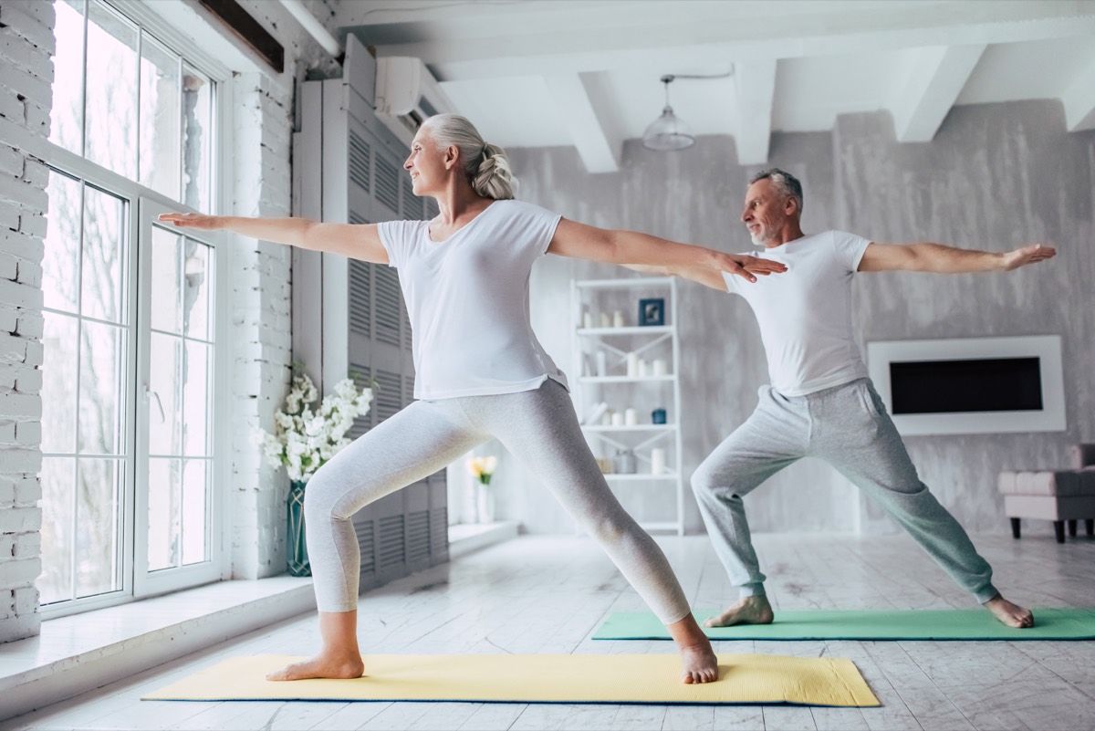 Mature couple practicing a standing yoga pose together at home.
